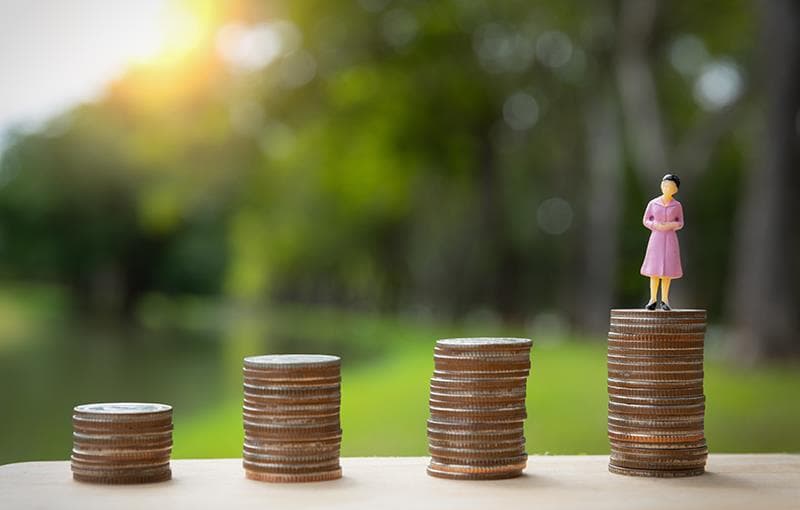 Stacks of coins growing taller, with a small figure standing on the highest stack